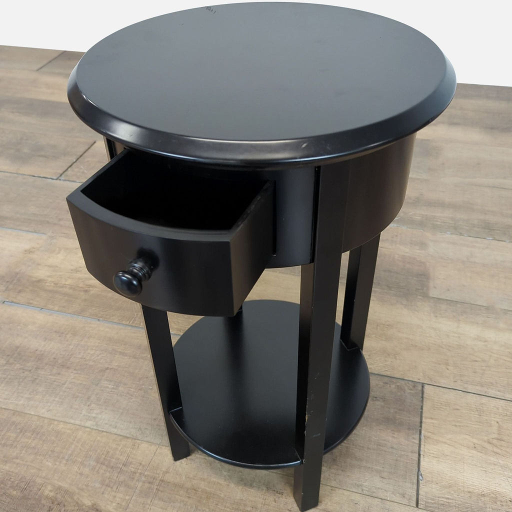 Close-up of Target black round side table with open drawer and lower shelf, shown at an angle.