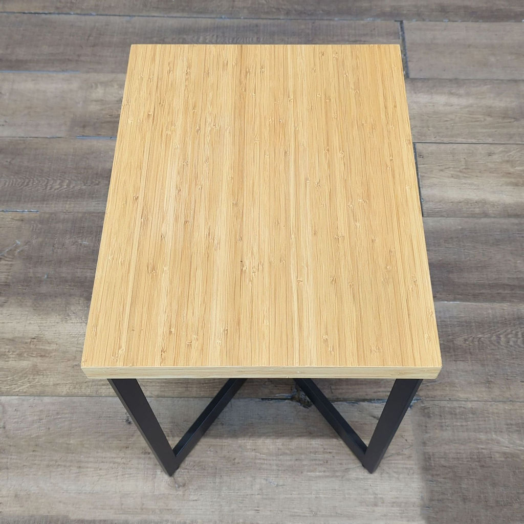 Top-down view of a Reperch side table showing a smooth light wood surface and sturdy black metal base.