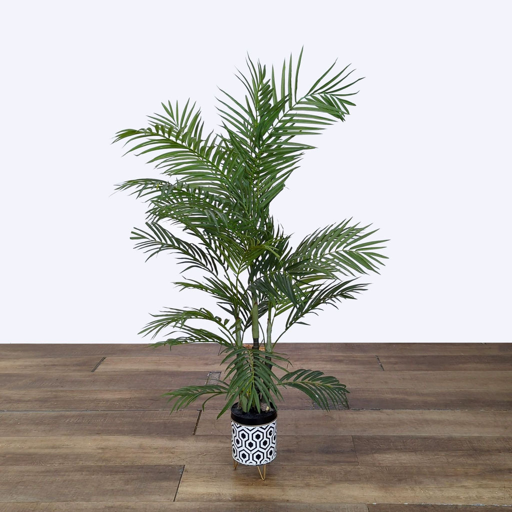 Tall artificial palm plant by Reperch in a black and white geometric pot stands on a wooden floor.