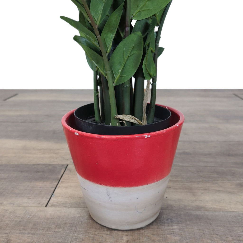 3. Bottom part of an artificial plant arranged in a red and white Reperch pot on a wooden floor.