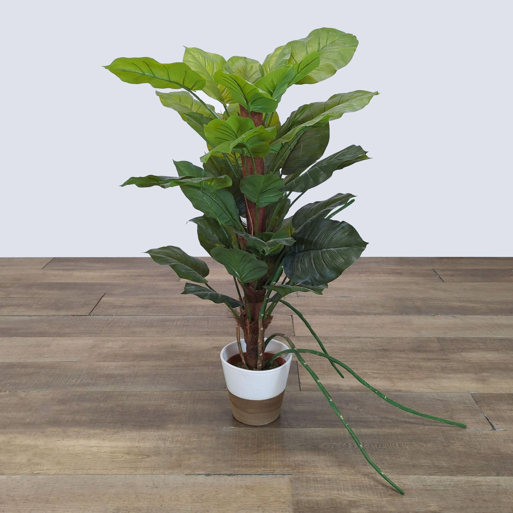 1. Tall artificial plant by Reperch in a white and tan pot, placed on a wooden floor, with broad green leaves.
