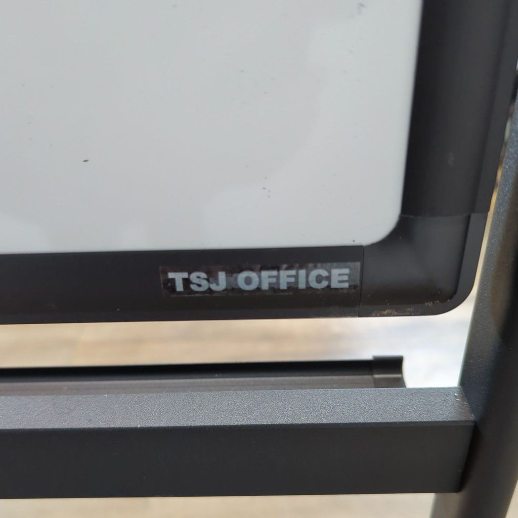 3. Close-up of the TSJ Office brand label on the corner of a magnetic whiteboard frame.