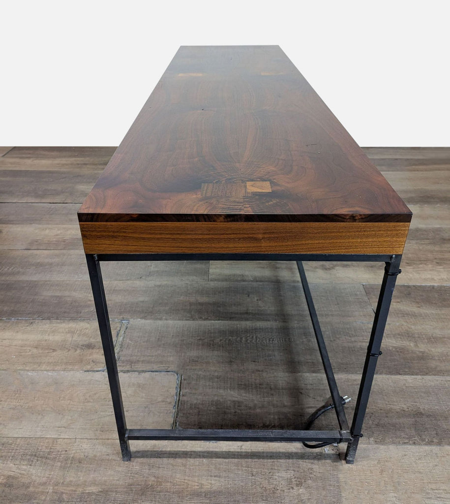 3. Side view of a Reperch desk, featuring a metal base, thick wood top, and cord visible near the legs.
