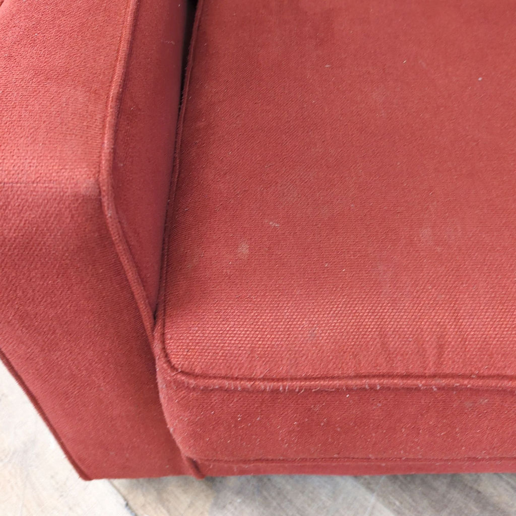 Close-up of the red fabric and stitching on the Reperch 3-seat sofa’s cushion and track arm.