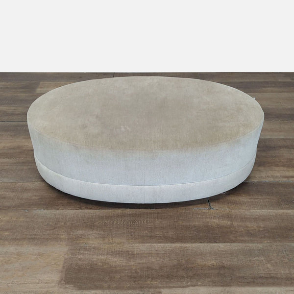 1. Oval-shaped, light beige upholstered ottoman from Reperch, placed on a wooden floor.
