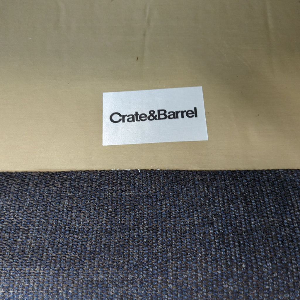 Close-up of a Crate & Barrel label on fabric upholstery, highlighting the brand of a lounge chair.