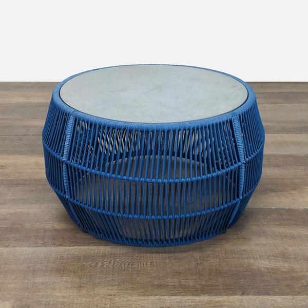 Blue rope-woven table by Reperch with a broad base and round stone top, shown on wood floor.  