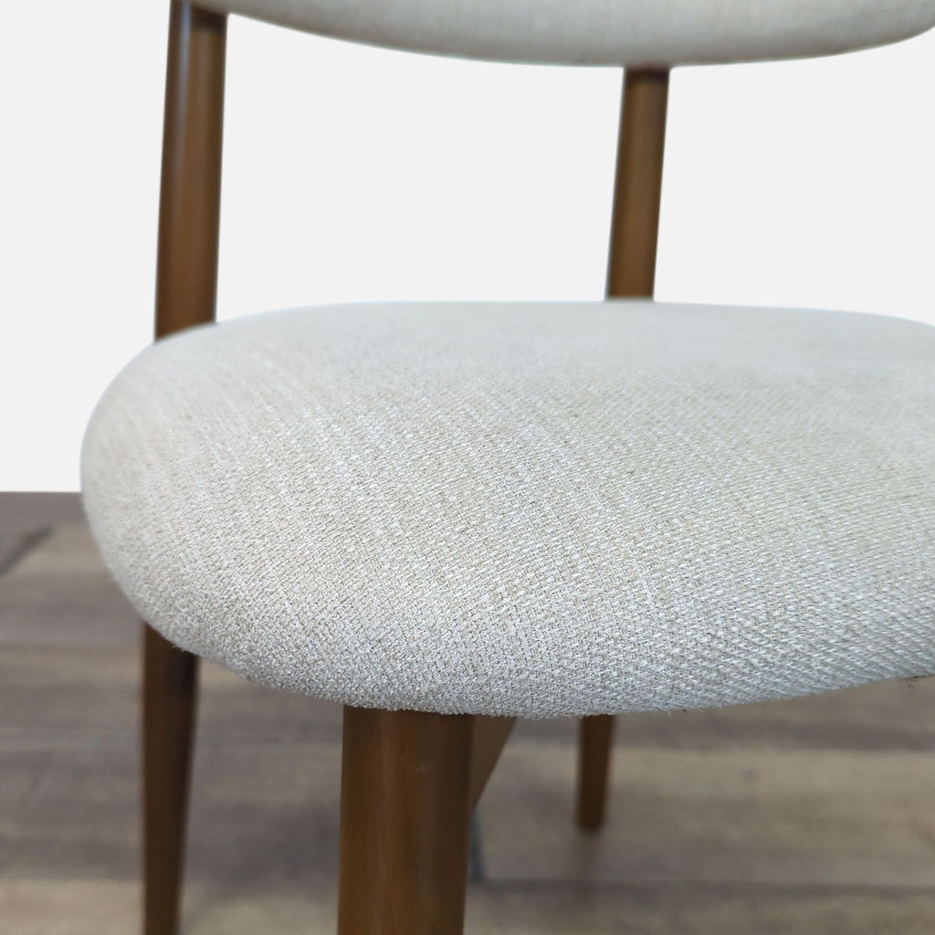 2. Close-up of the West Elm dining chair's textured fabric seat and wood frame, showing the upholstery detail.  