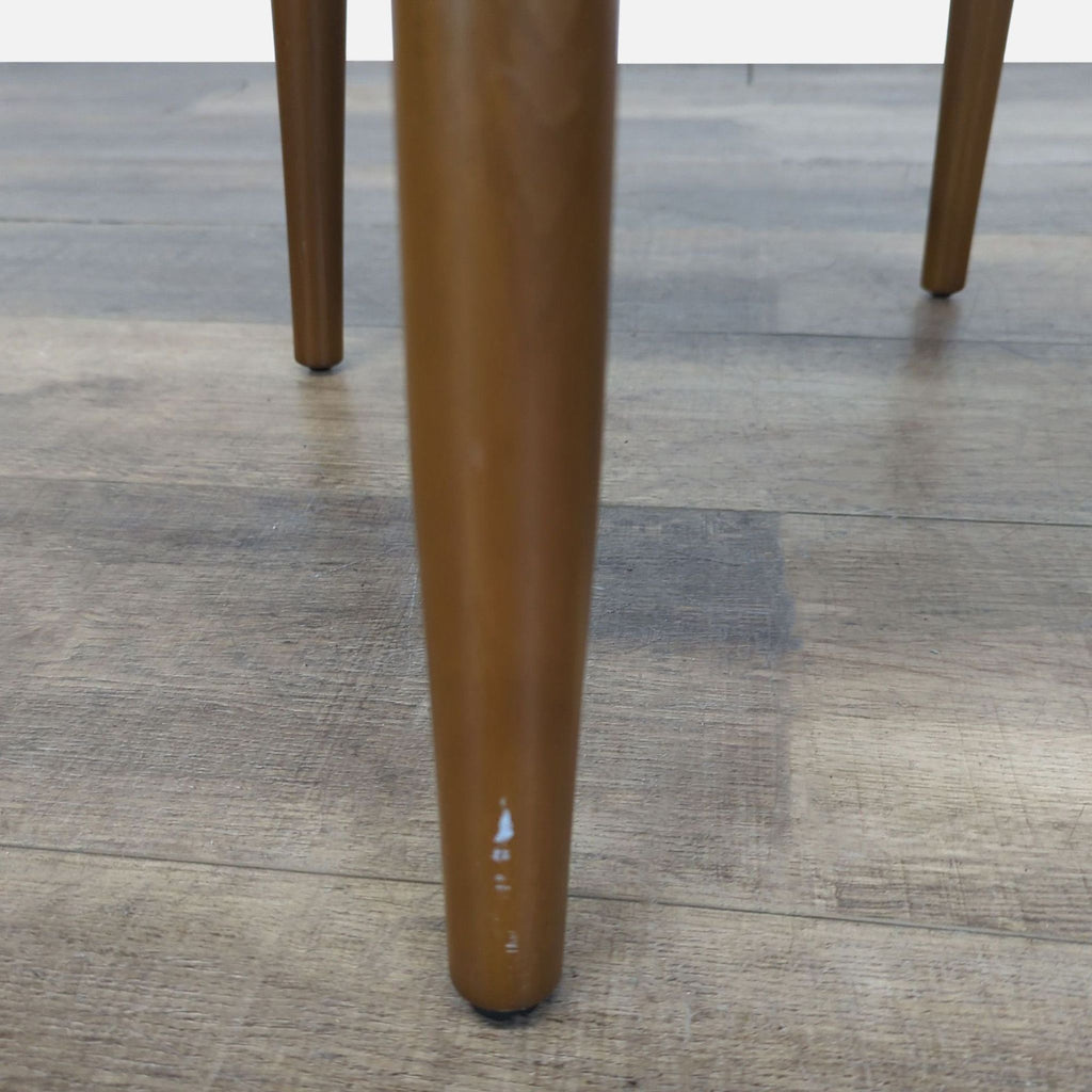 3. Detail of a wooden leg from a West Elm dining chair in the Dining Chairs category, with slight wear visible.