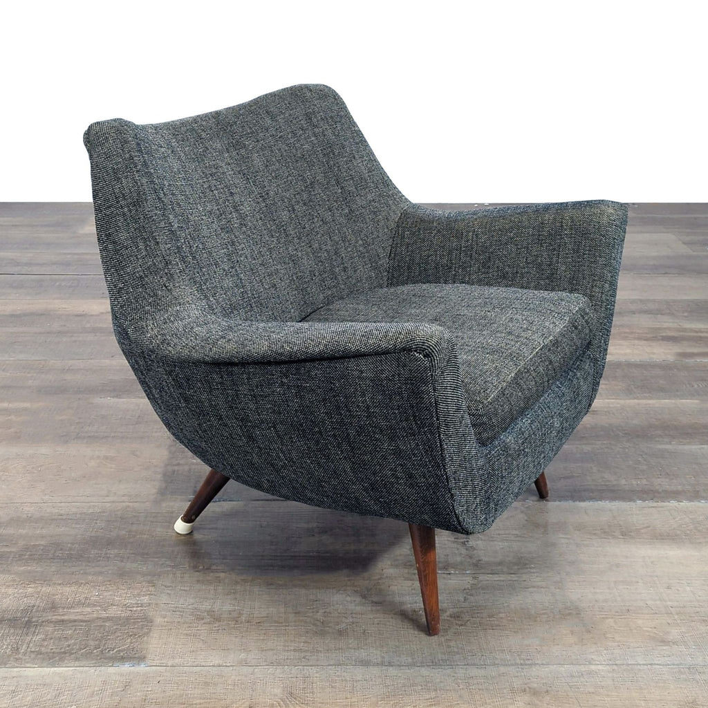 Angled side view of a Reperch lounge chair, showing its gray tweed fabric and dark wooden legs.