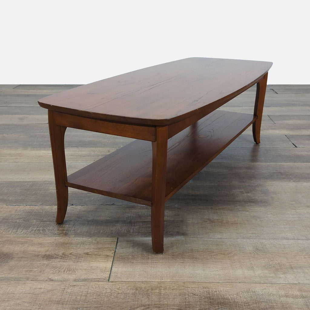 2. Angled view of a wooden Pottery Barn coffee table featuring flared legs and smooth, rounded edges.