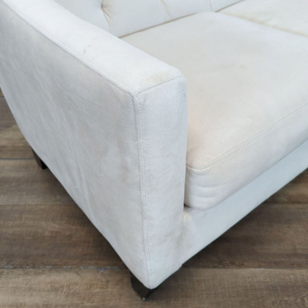 1. Close-up of a light-colored upholstered armrest and seat from Ashley Furniture, shown on a wood floor.