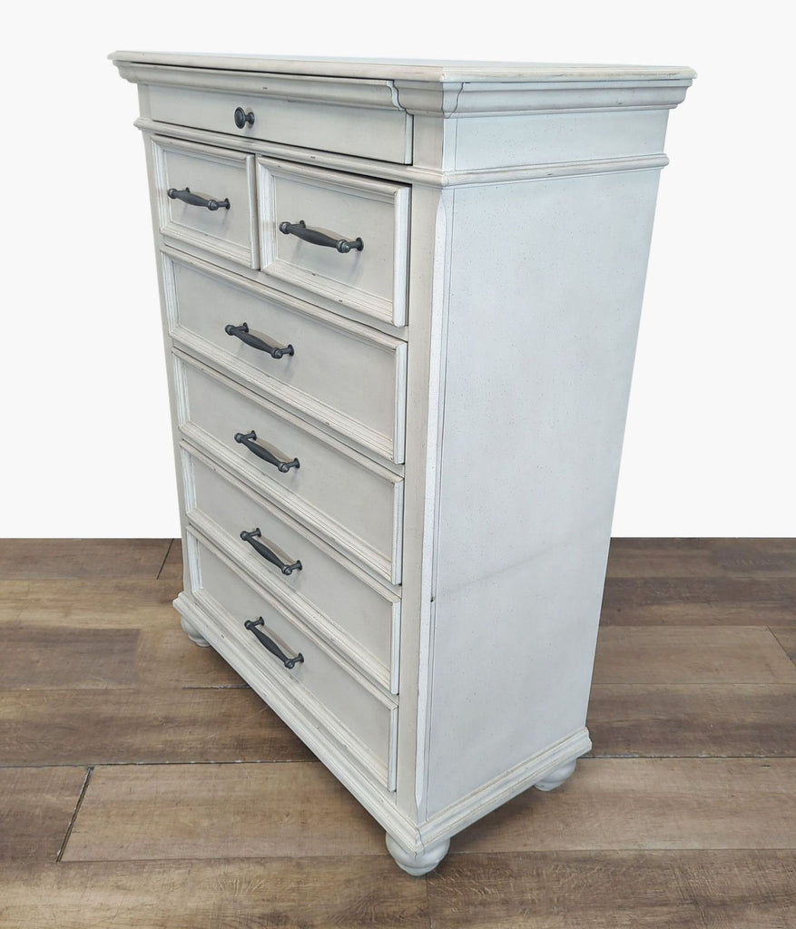 2. Angled view of a white Ashley dresser showing elegant molding, five drawers with dark handles, and bun feet.
