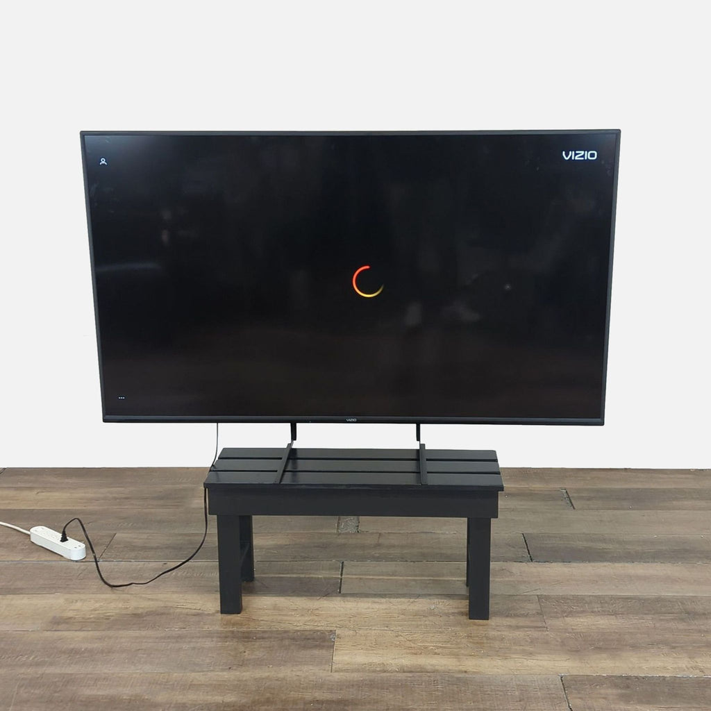 A large Reperch TV with thin bezels sits on a black stand, displaying a loading screen in a modern room.