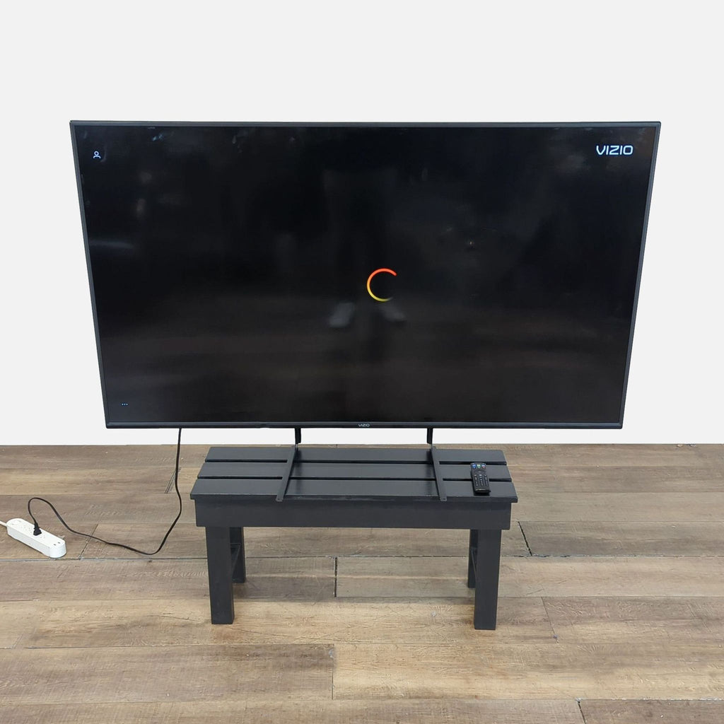 2. Vizio V655-H19 65-inch TV on a black bench, screen showing loading icon, remote placed on the stand.