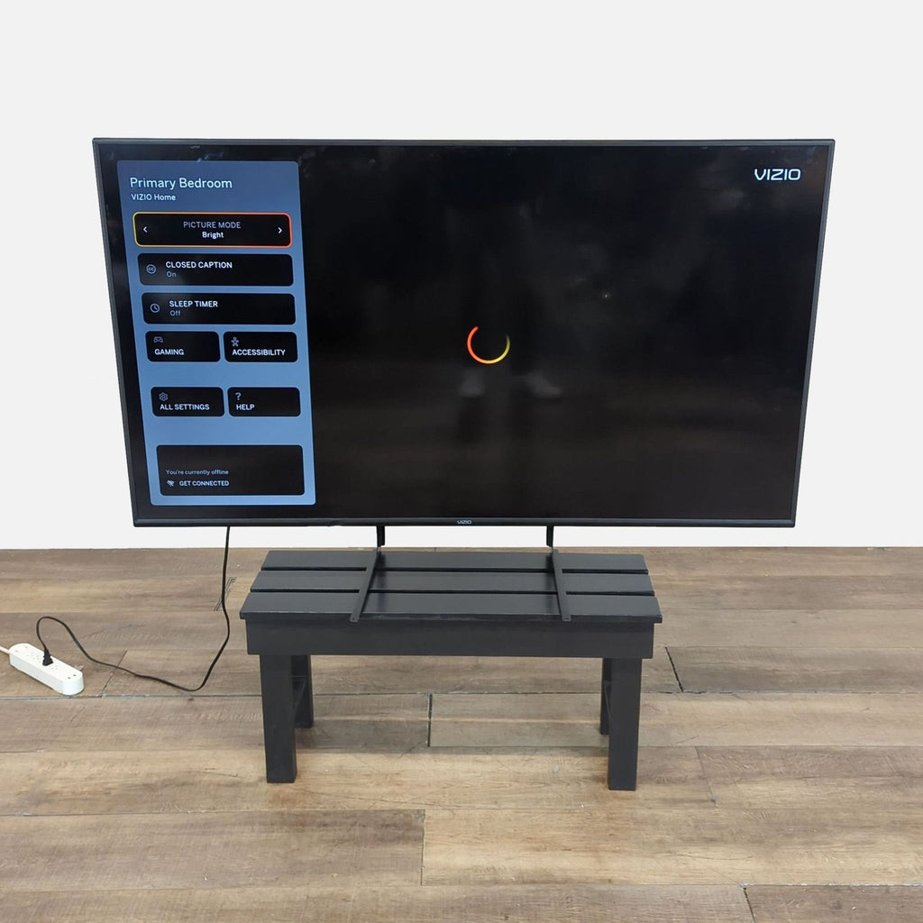 1. Vizio V655-H19 65-inch 4K Smart TV displaying menu options, set on a small black stand with power strip.