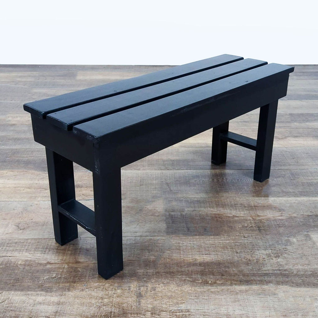 2. Angle view of a black Reperch slatted bench, sturdy legs and clean lines, placed on a wood floor.  