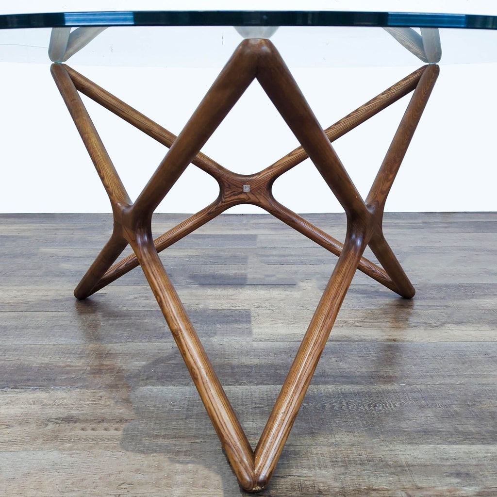 3. Close-up of a walnut-stained ash base supporting a round glass dining table, modern design by Nuevo.