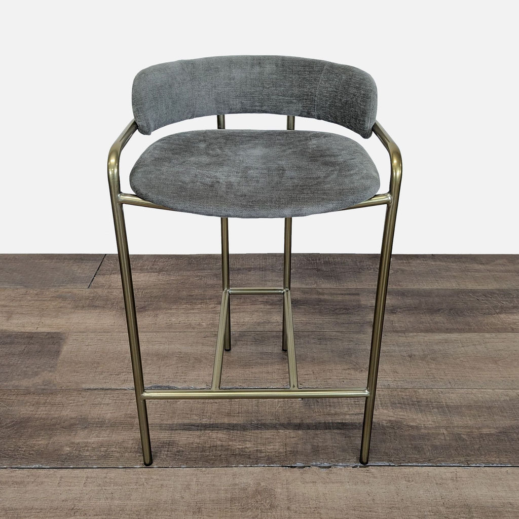 1. Front view of a West Elm Lenox Counter Stool featuring gray upholstery and a brass metal frame on wooden flooring.