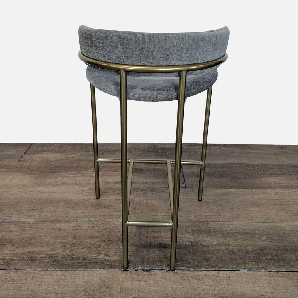 2. Rear view of a West Elm Lenox Counter Stool showing curved gray backrest and brass frame legs on wood floor.