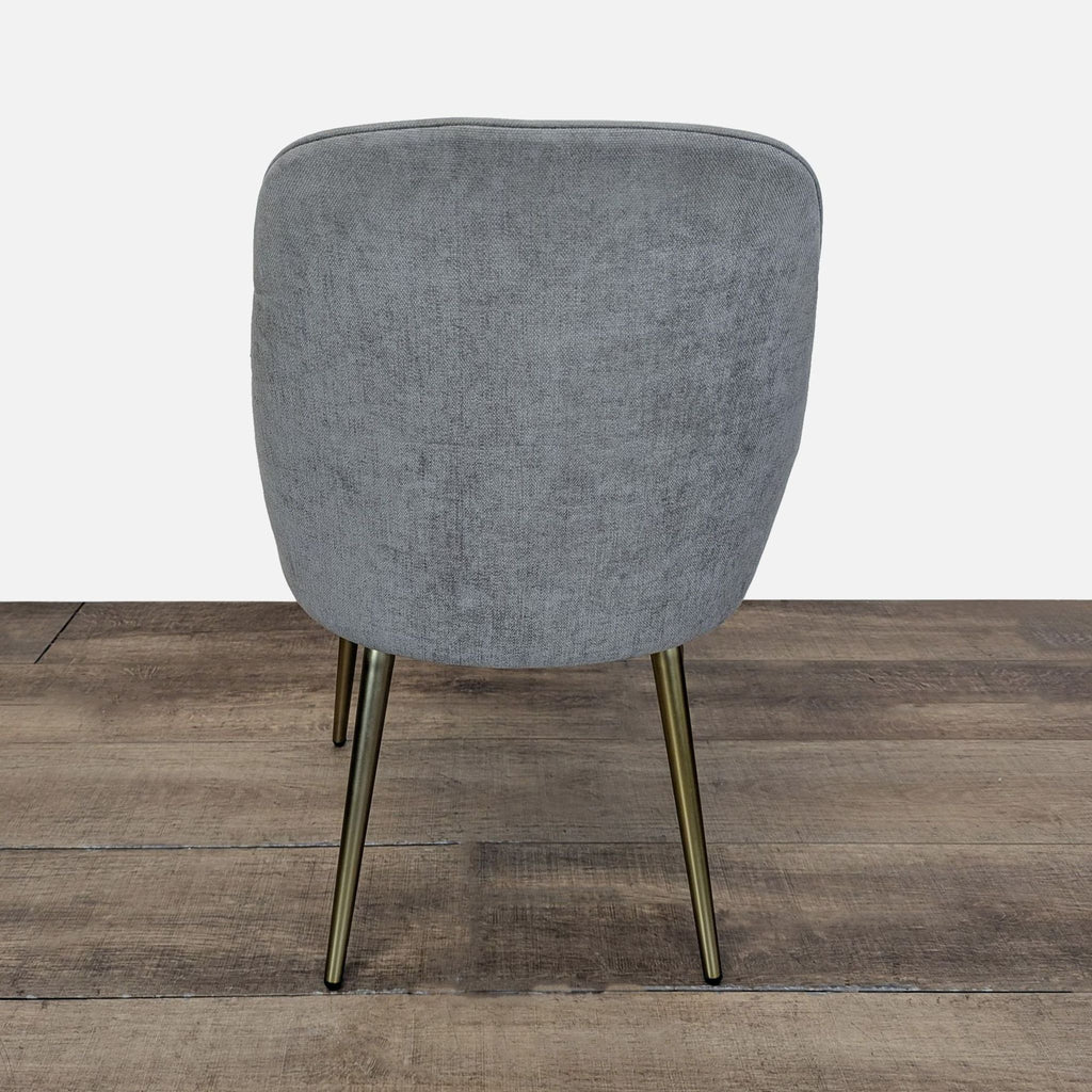 2. Rear view of West Elm dining chair in grey velvet upholstery and brass legs, set on a wooden floor.  