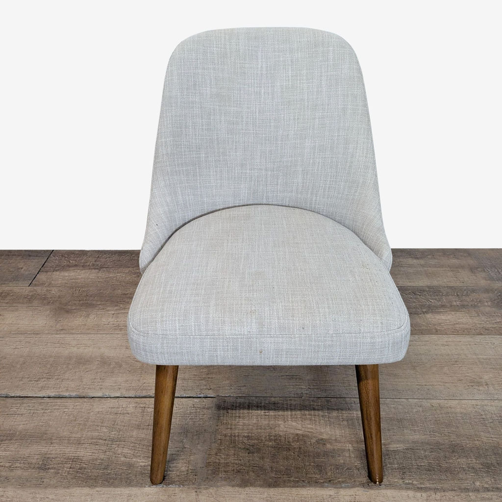 1. Front view of a West Elm dining chair with light grey fabric upholstery and wooden legs on a wooden floor.