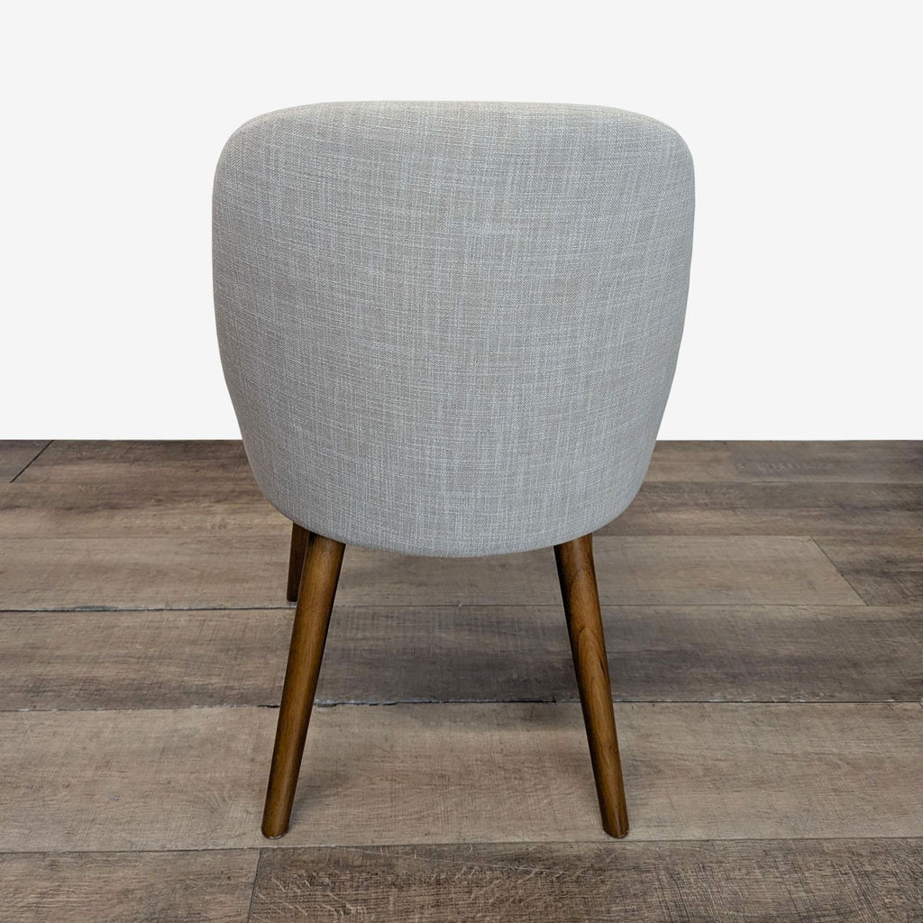 2. Rear view of a West Elm dining chair showing curved, upholstered backrest and four angled wooden legs.