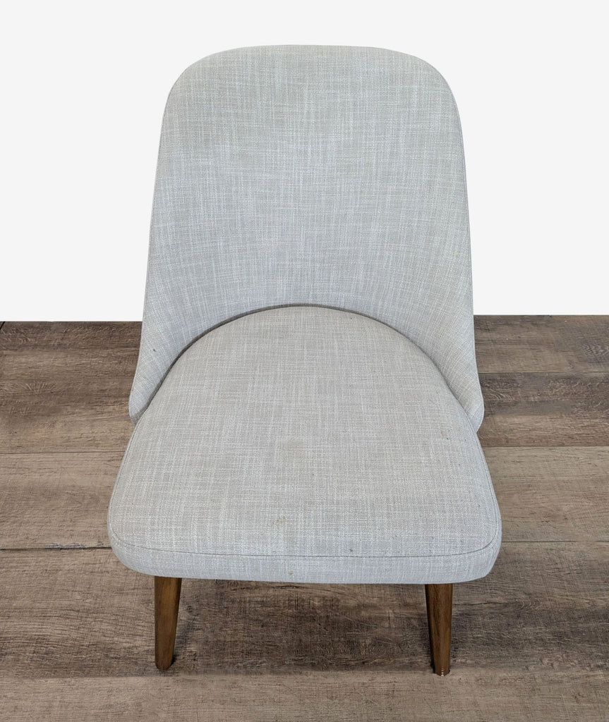 3. Angled front view of a West Elm dining chair with soft grey textured fabric and tapered wood legs, on wood flooring.