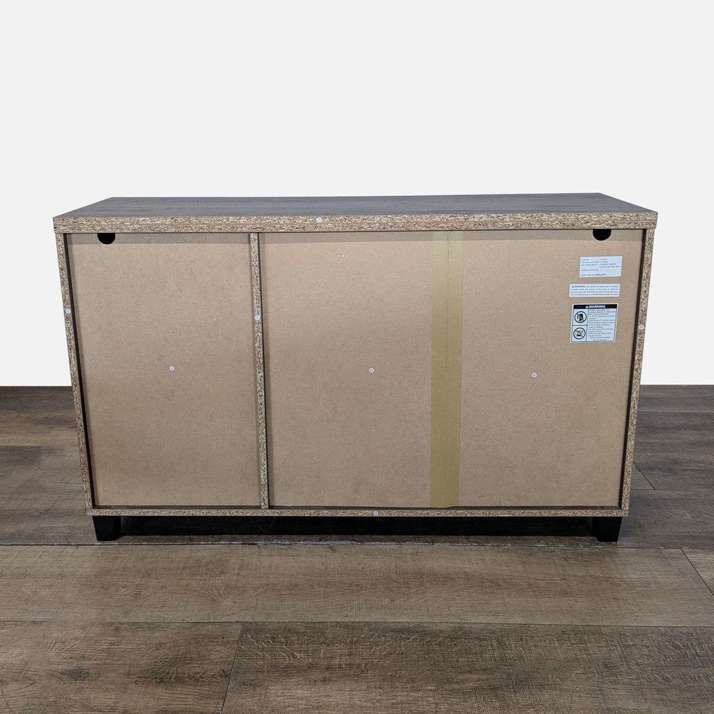 3. Back view of the Synergy House cabinet, featuring a plain unfinished wood particleboard panel.