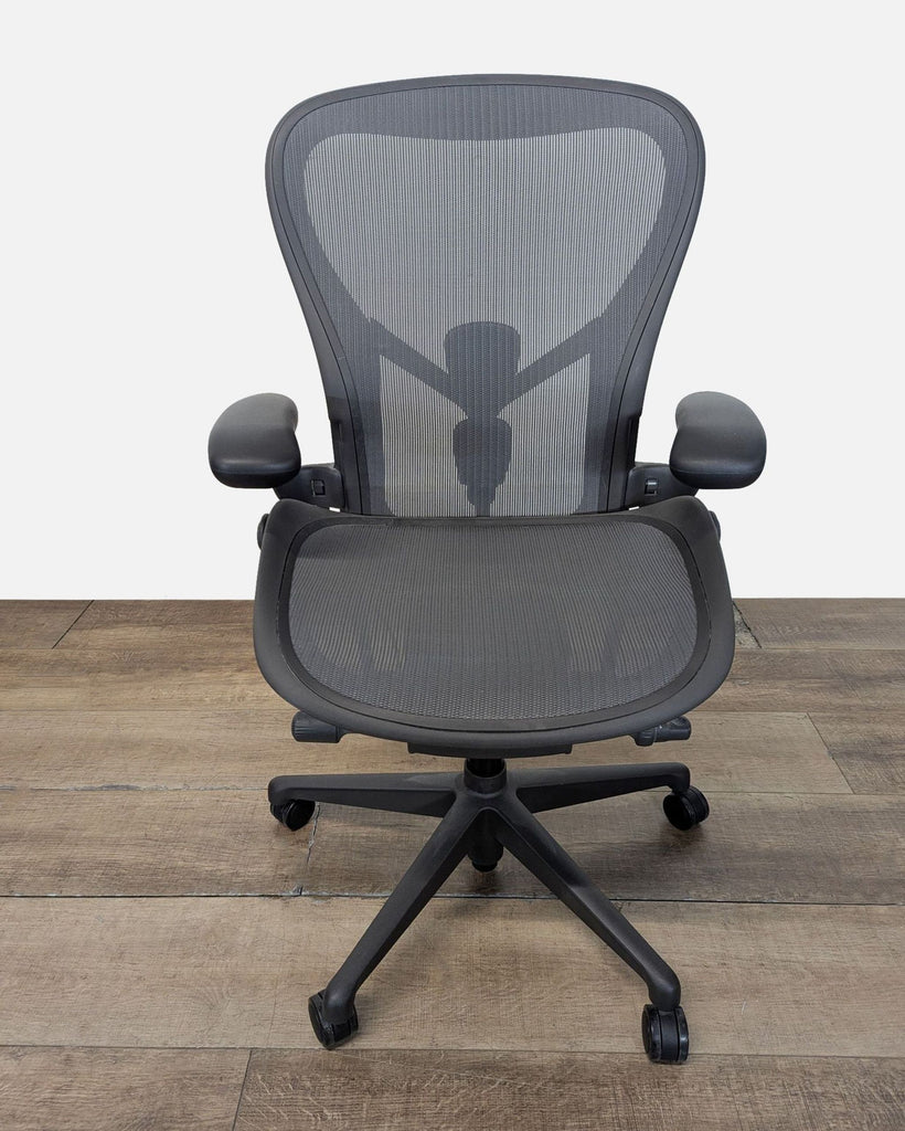 1. Front view of a Herman Miller ergonomic office chair with mesh back, adjustable arms, and lumbar support on wood floor.