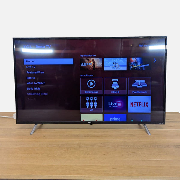 1. TCL 40-inch Roku Smart TV on a wooden table, showing its smart home interface and streaming apps.