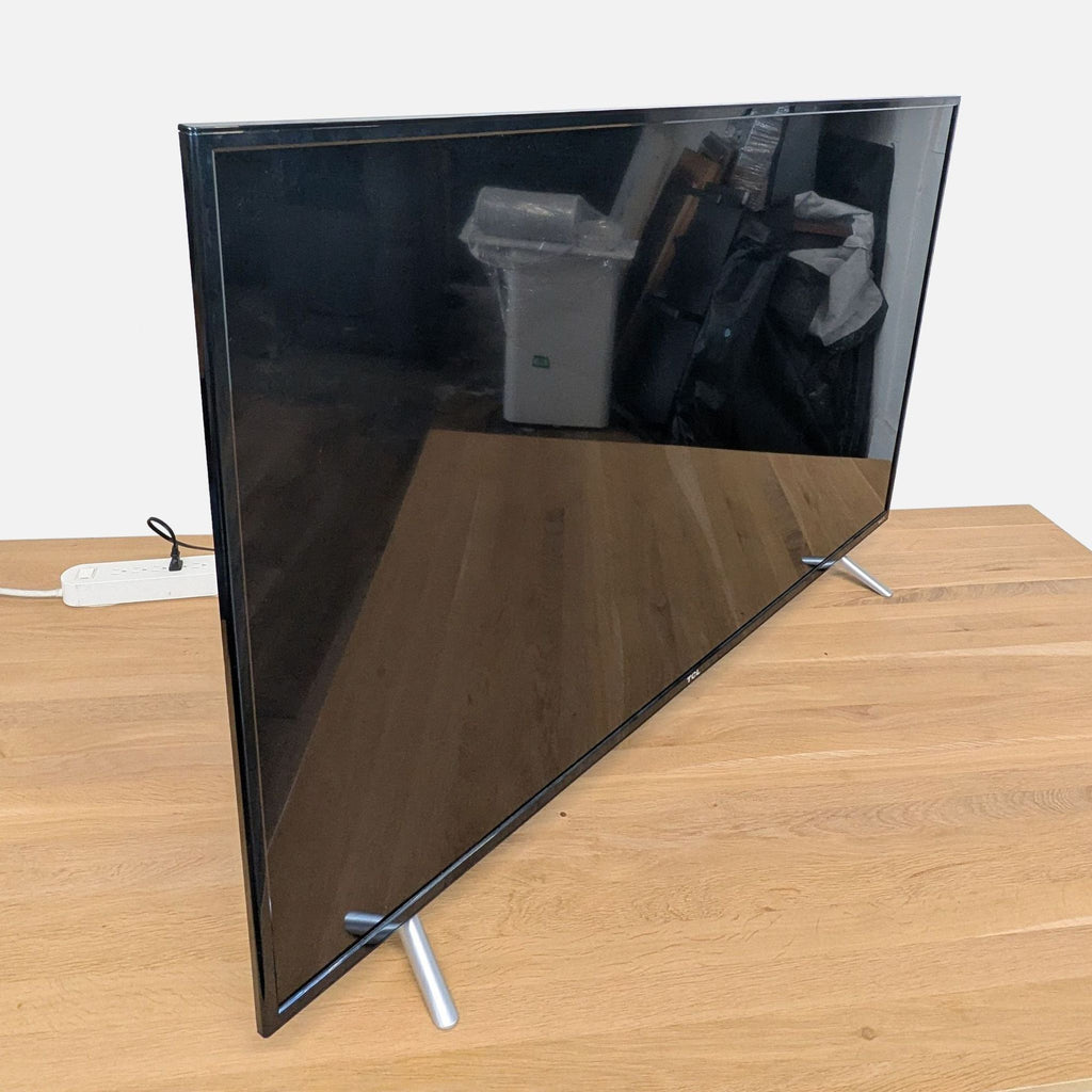 2. Side view of a TCL 40-inch TV with a slim, modern design and sturdy legs on a wooden table.
