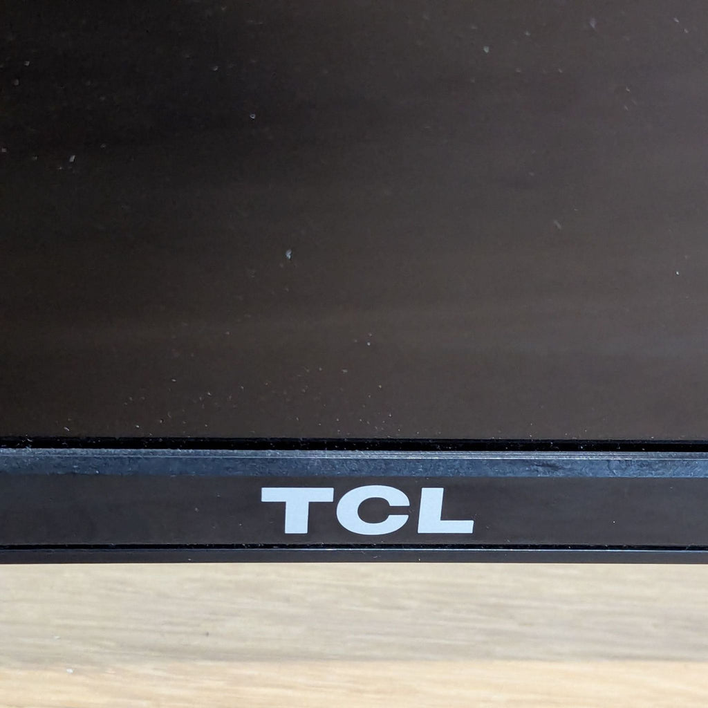 3. Close-up of the bottom bezel of a TCL TV, displaying the TCL brand logo on a black frame.