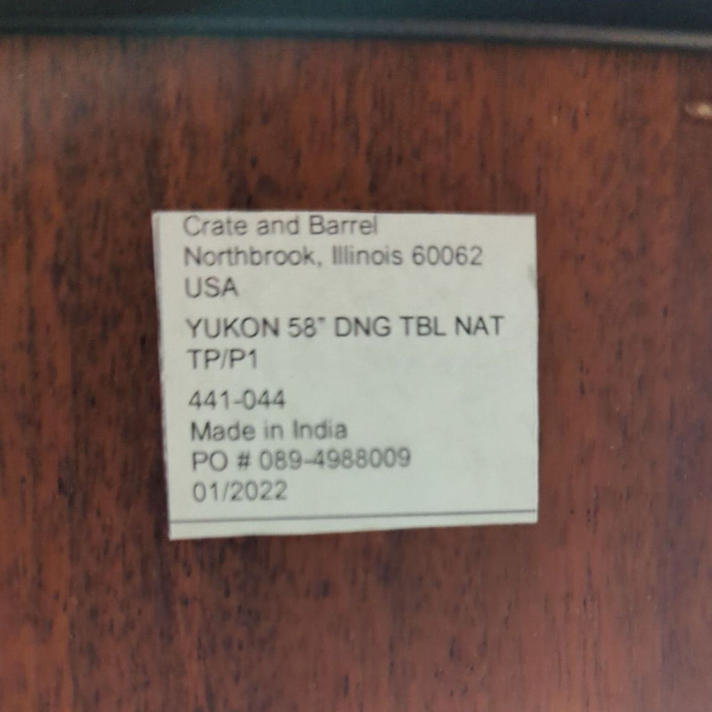 Crate and Barrel product label reading "YUKON 58'' DNG TBL NAT," made in India, on wood surface.