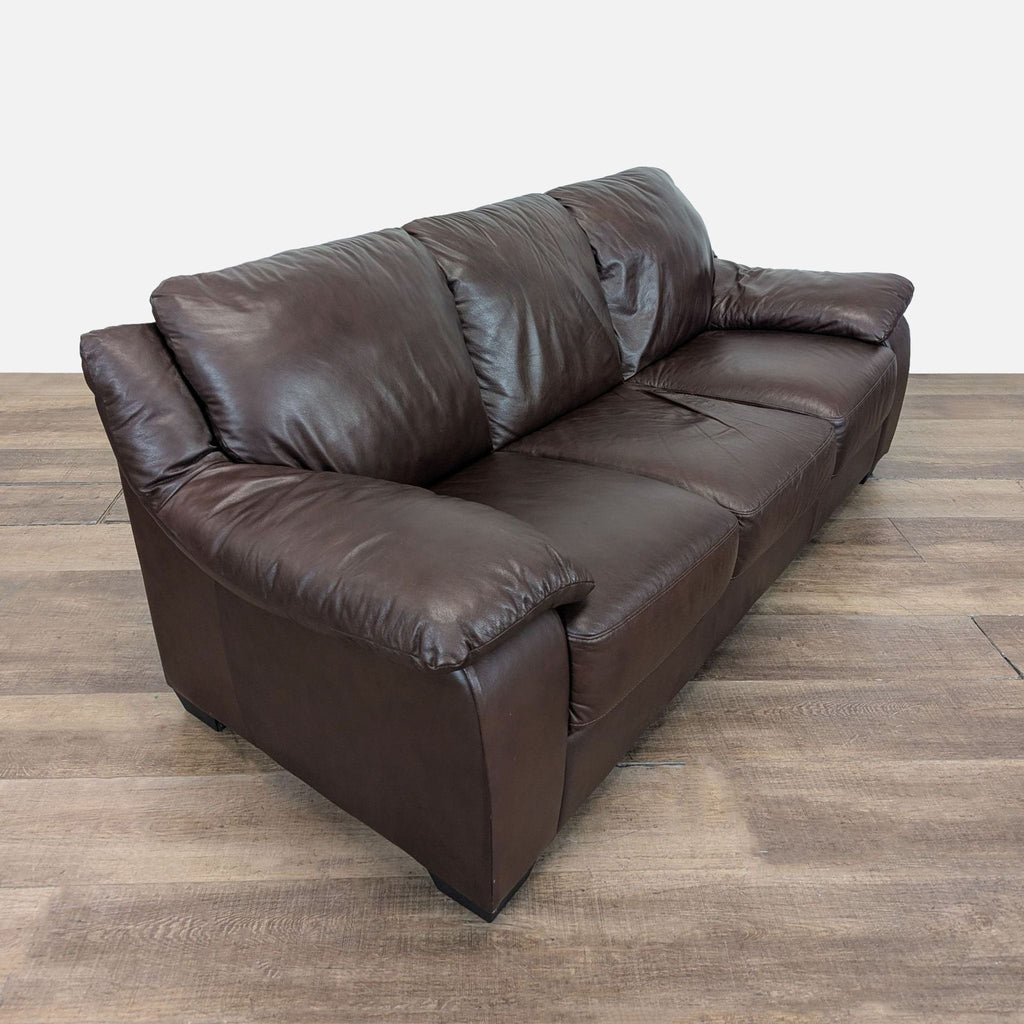 2. Angled side view of a brown leather Natuzzi 3-seat sofa with overstuffed cushions.