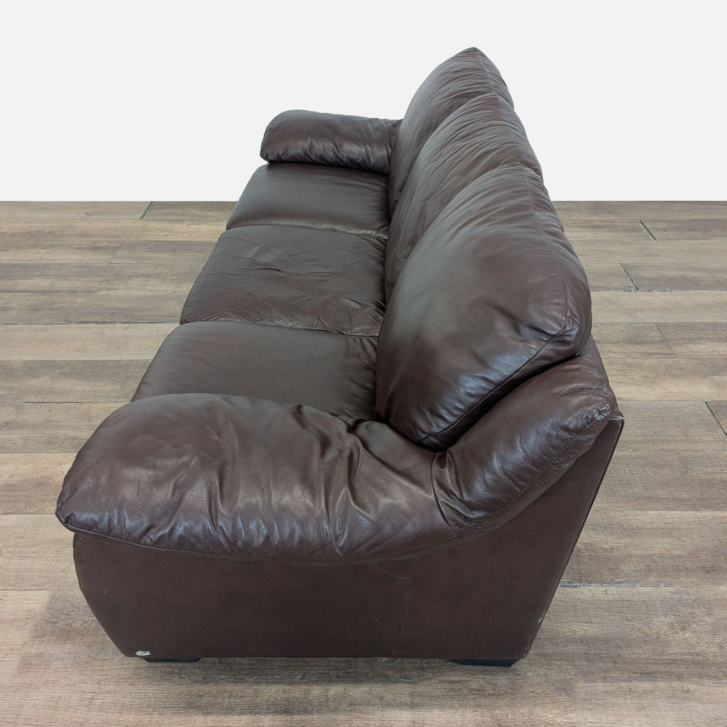 3. Side profile of Natuzzi 3-seat sofa featuring plush brown leather cushions and wide armrests.