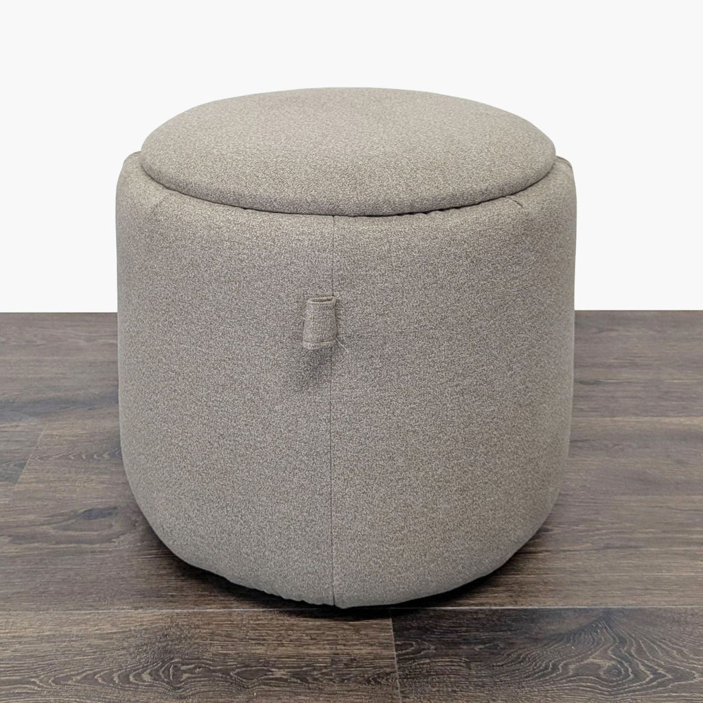 1. Round beige Ikea ottoman with a soft fabric finish, placed on dark wood flooring, lid closed.  