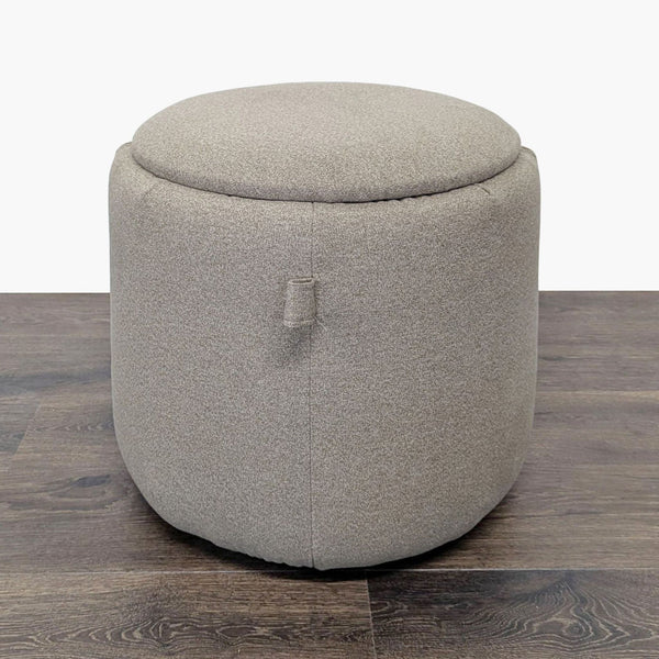 1. Round beige Ikea ottoman with a soft fabric finish, placed on dark wood flooring, lid closed.  