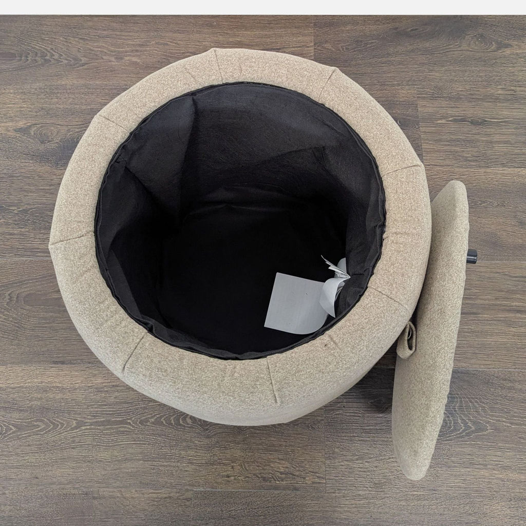 3. Top view of an open round beige Ikea ottoman showing its black-lined storage compartment and detached lid.