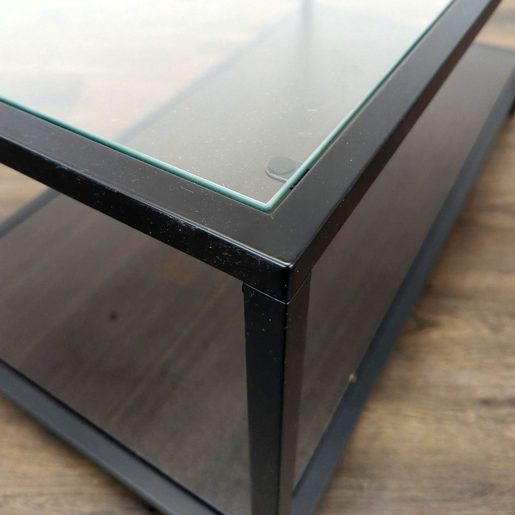 Corner detail of the Reperch coffee table showing the glass top and black metal frame from a side angle.