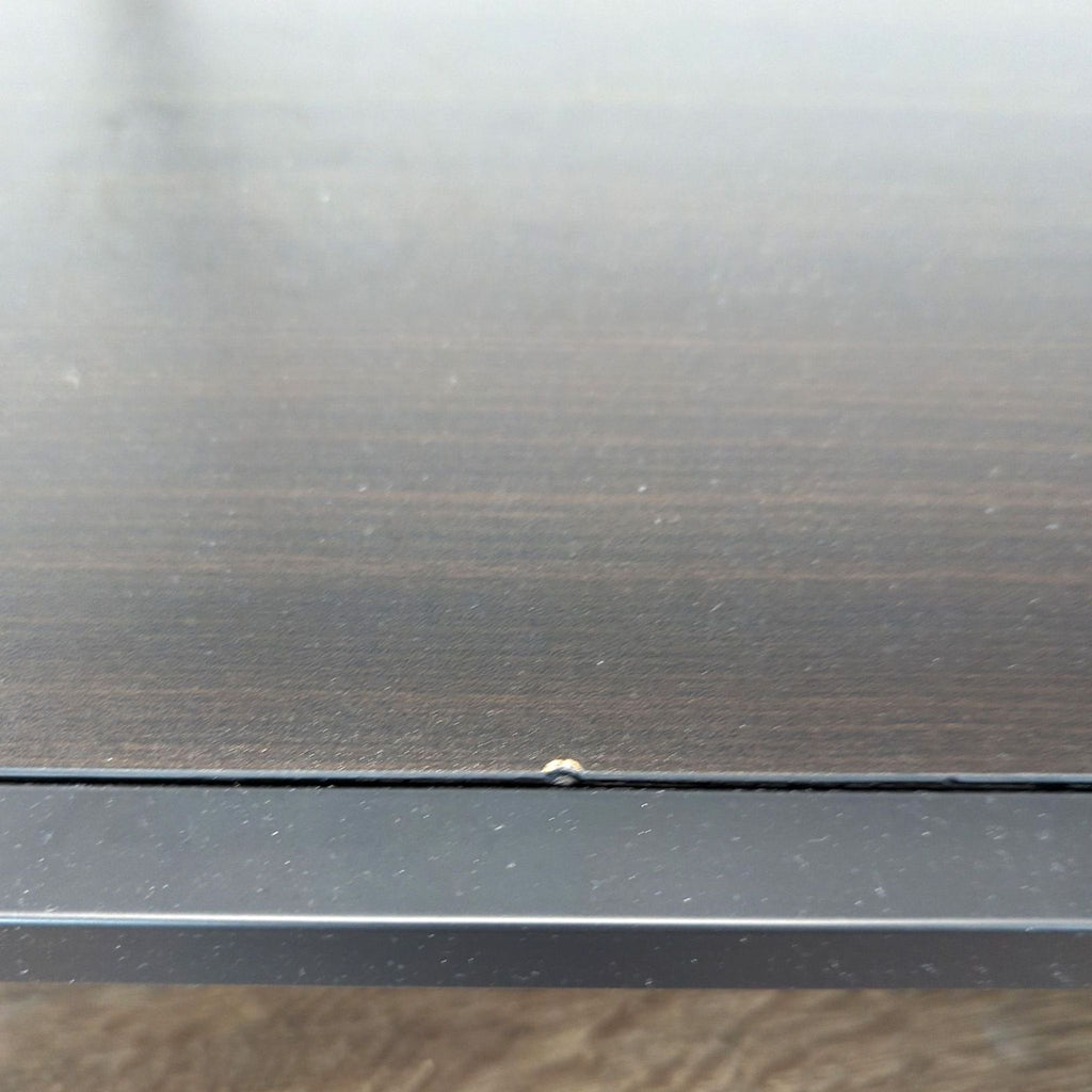 Close-up of the lower black shelf of a Reperch coffee table with a small defect on the edge surface.  