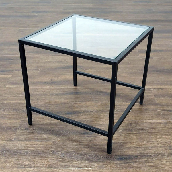 1. Square Reperch side table with black metal frame and glass top on wood floor background.
