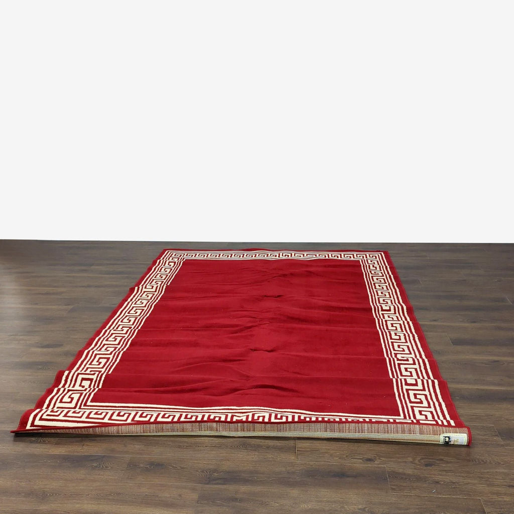 3. Full view of a large red Taj Mahal rug with a Greek key border, positioned on a dark wooden floor.