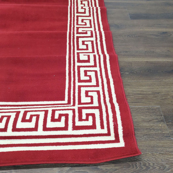 1. Close-up of a red Taj Mahal rug featuring an ivory Greek key border design, placed on a wooden floor.