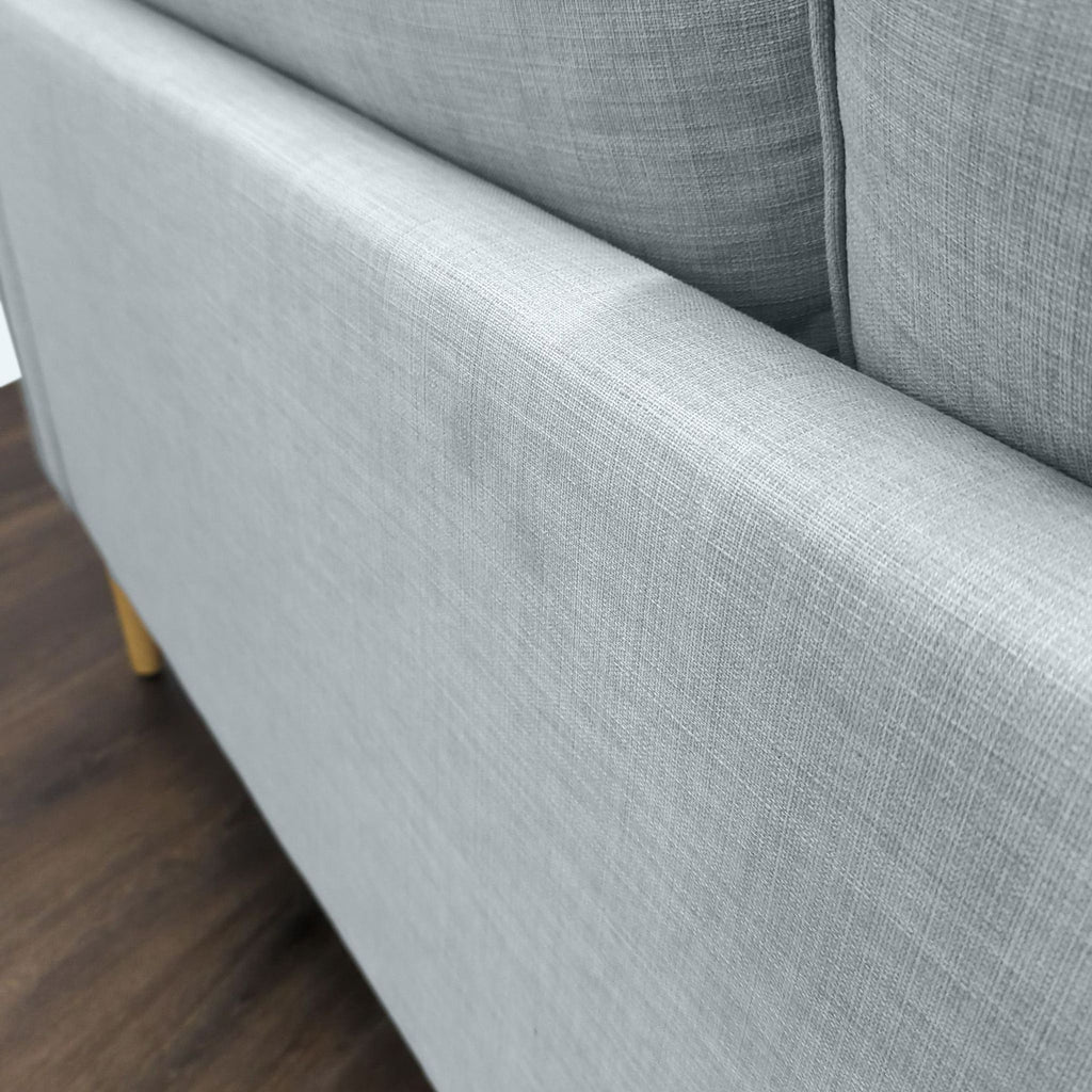 2. Detailed side view of the Reperch Loveseat shows its smooth, light gray upholstery and wooden legs.