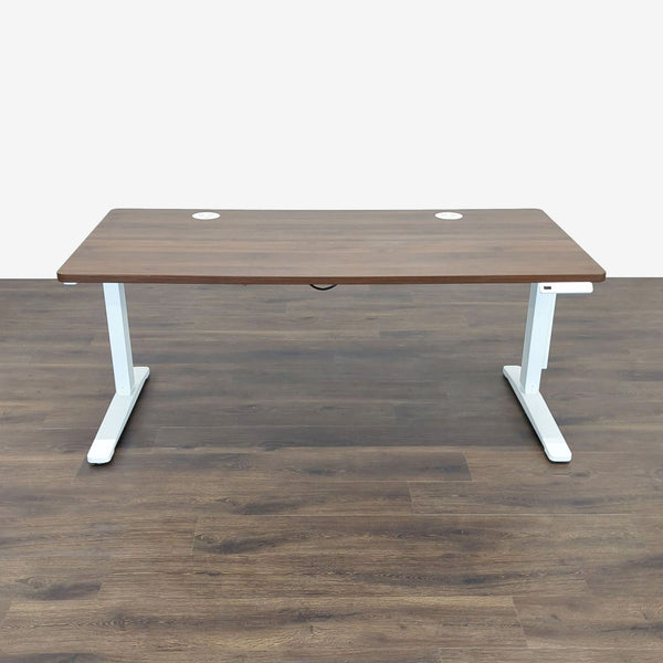 Wide walnut-finish UPLIFT desk with white electric adjustable frame and built-in power grommets for workspace organization.  