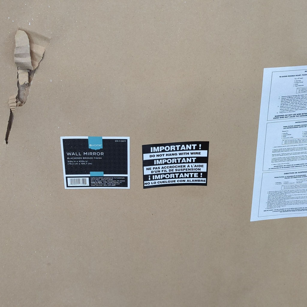 Backside of Target Home mirror showing manufacturer label, warning stickers, and a tear in the brown paper cover.  