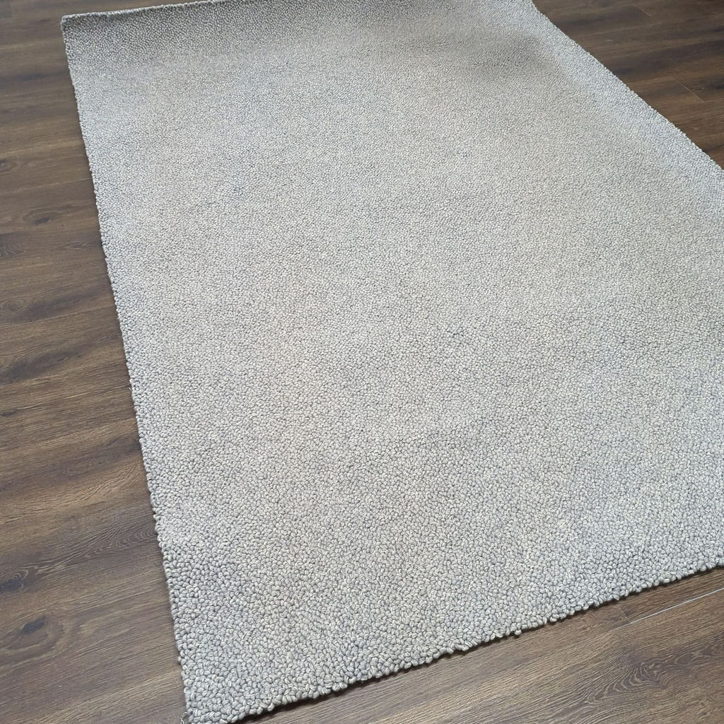 2. Full view of a light gray, pebble-textured Room & Board rug laying flat on wood floors.  