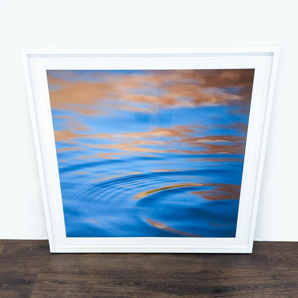 1. Framed Reperch print of abstract blue water and golden reflections, leaning against a white wall on wood floor.