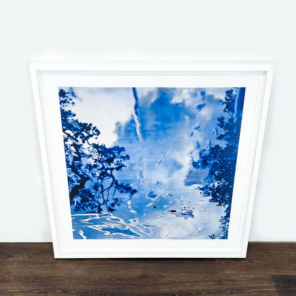 1. Framed blue and white abstract print by Reperch, featuring water and tree reflections, leaning on a wall.